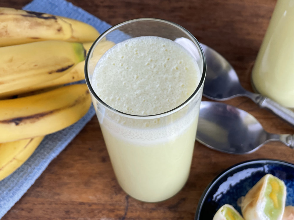 Banana milk in a glass with bananas in the background