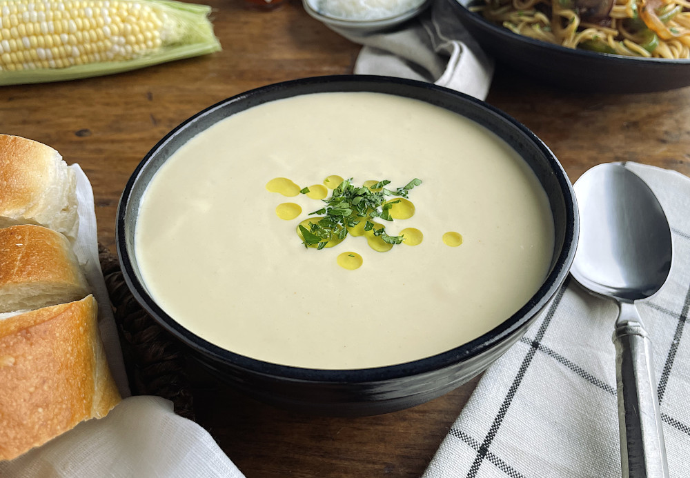 Corn potage in a black bowl with a spoon on the side