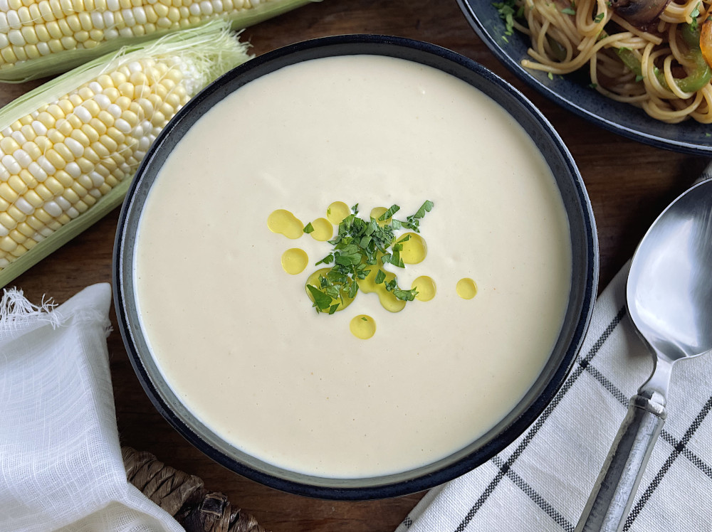 Corn potage in a black bowl with corn cobs in the background