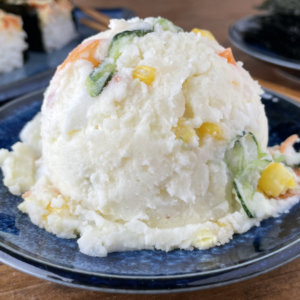 Japanese Potato Salad with carrots, cucumber and kewpie on a small plate with sushi bake in background
