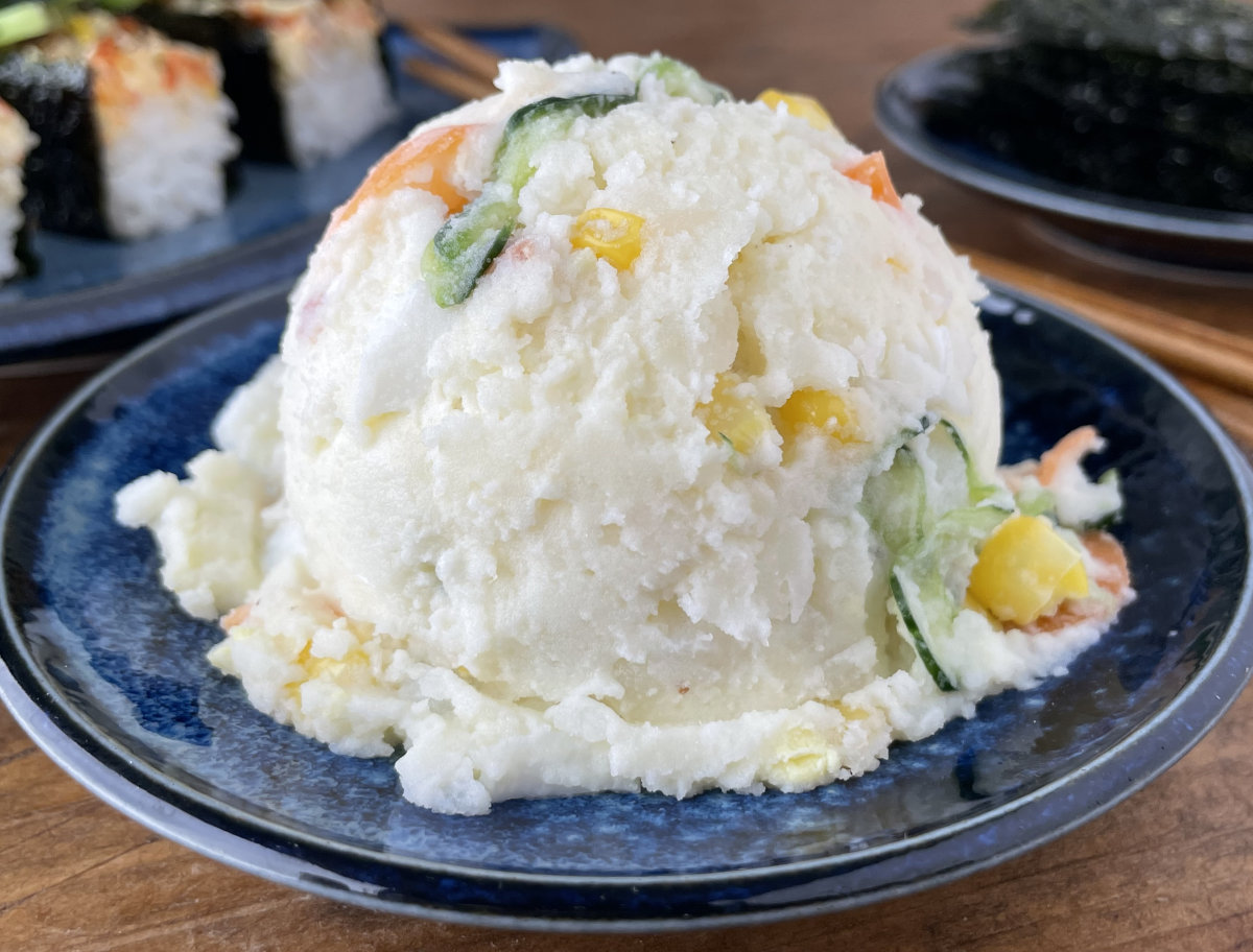 Japanese Potato Salad with carrots, cucumber and kewpie on a small plate with sushi bake in background