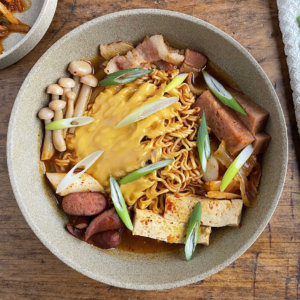 Korean Army Stew in tan bowl with green chopsticks and napkin on side