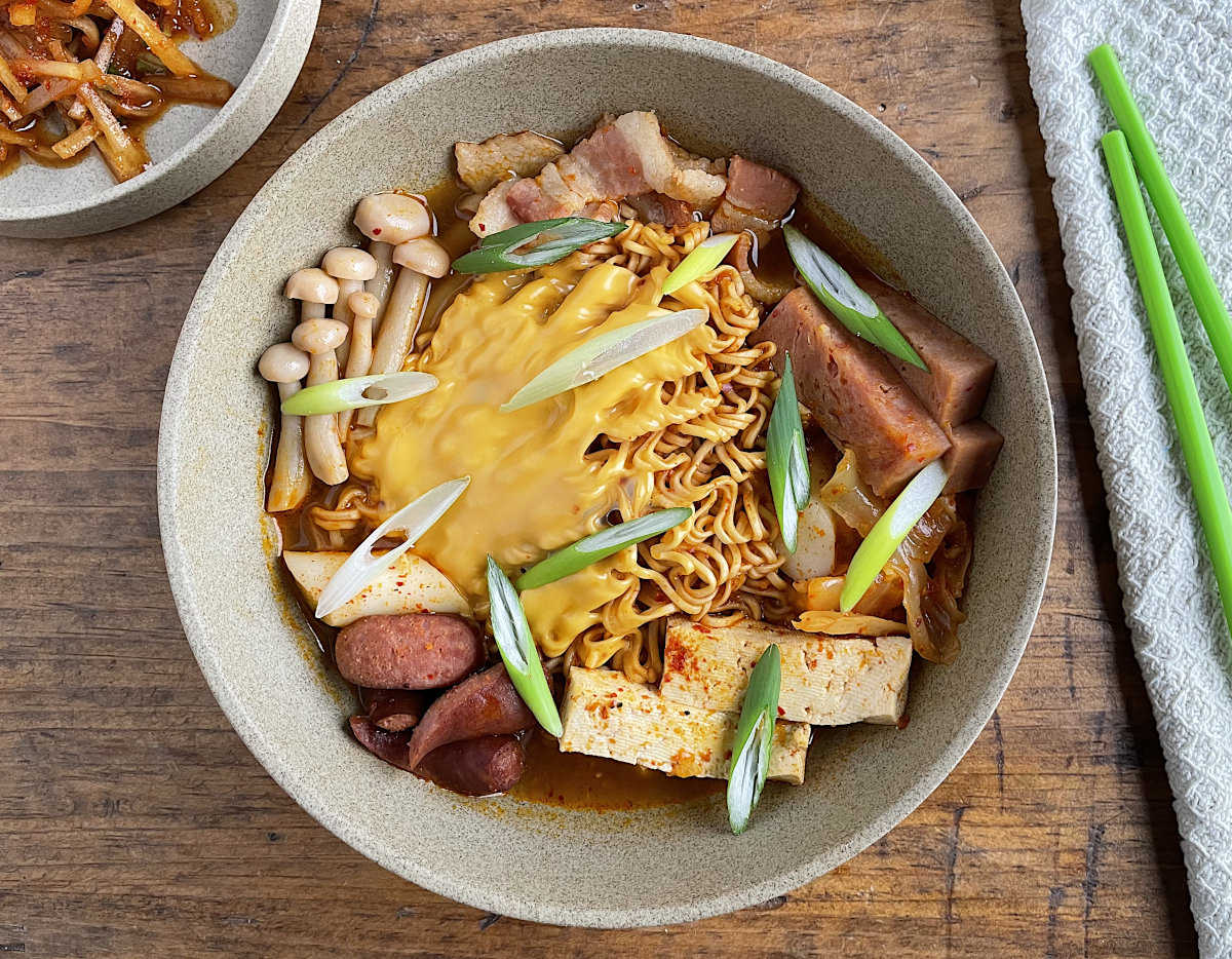 Korean Army Stew in tan bowl with green chopsticks and napkin on side