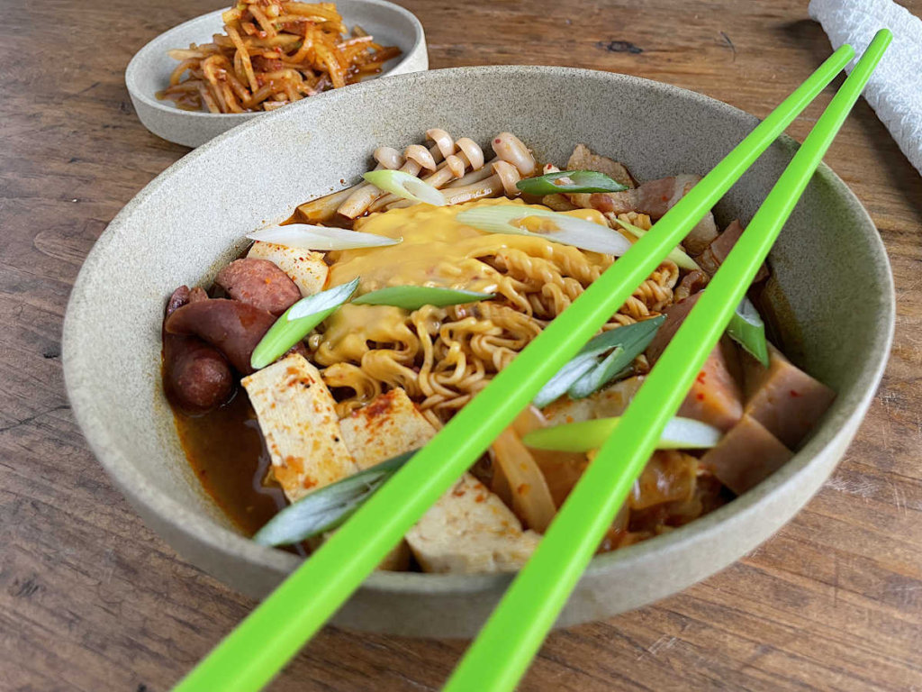 Korean Army Stew with green chopsticks on top of bowl