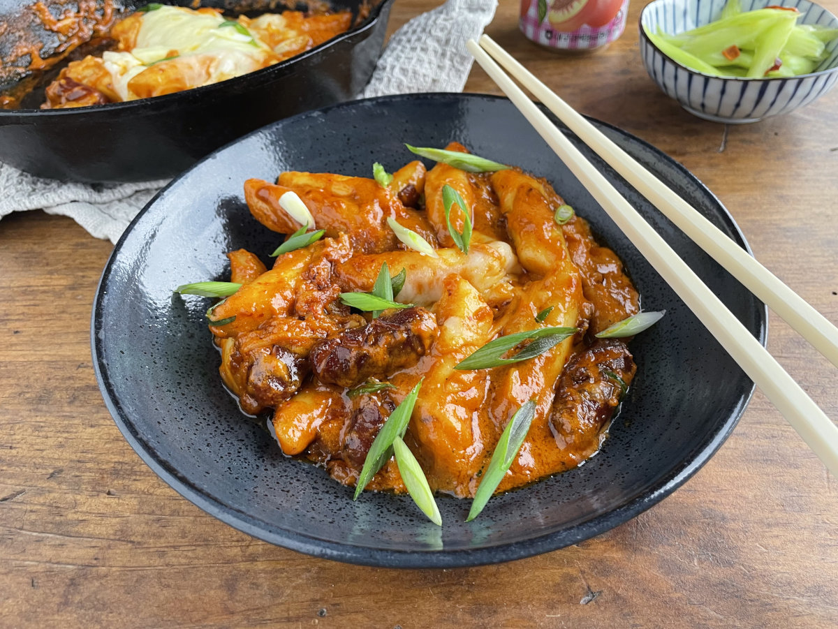 Rose tteokbokki in bowl with cast iron pan in background