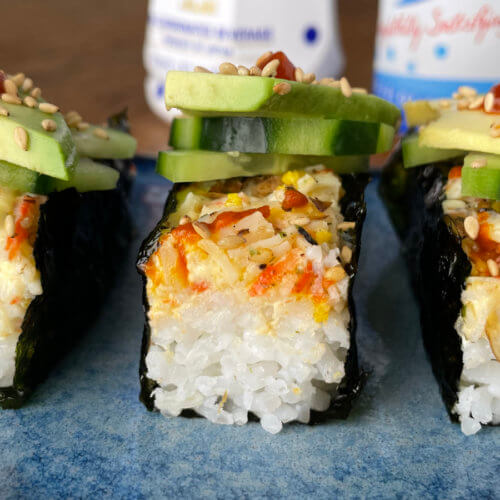 sushi bake wrapped in seaweed with cucumbers, avocado, sesame seed and sriracha on top