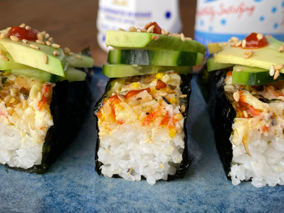 sushi bake wrapped in seaweed with cucumbers, avocado, sesame seed and sriracha on top