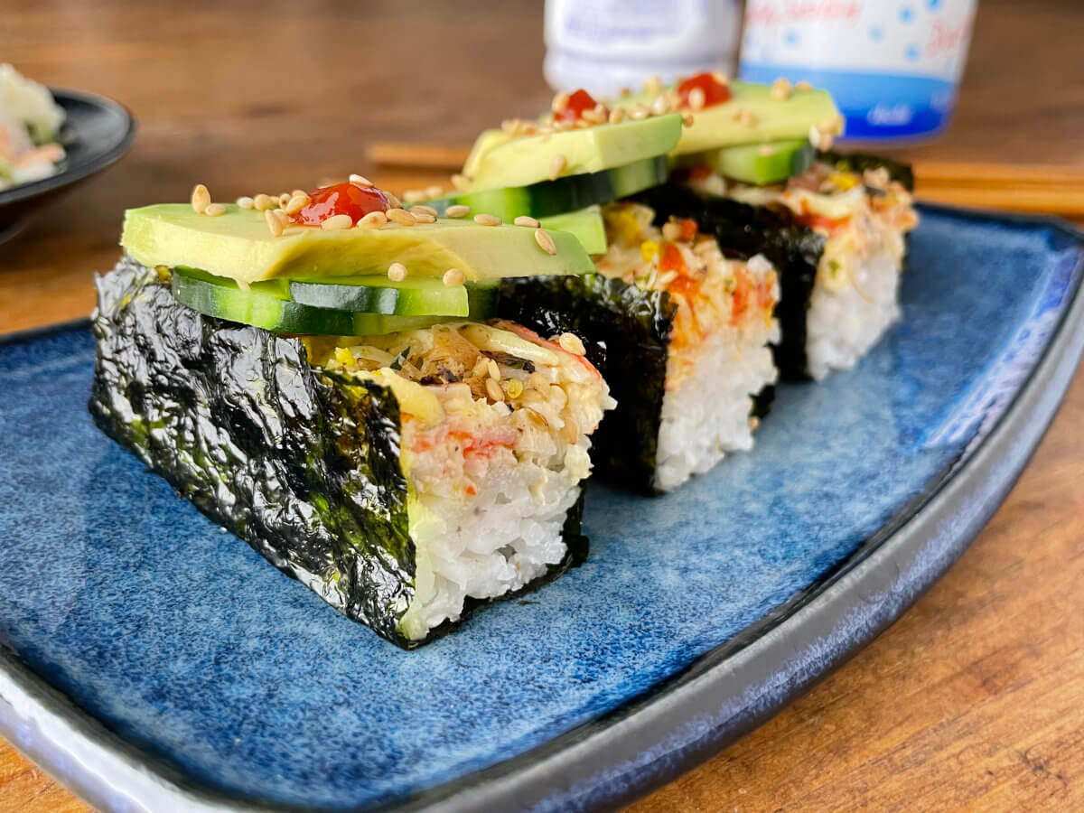 sushi bake wrapped in shiny seaweed topped with cucumber and avocado