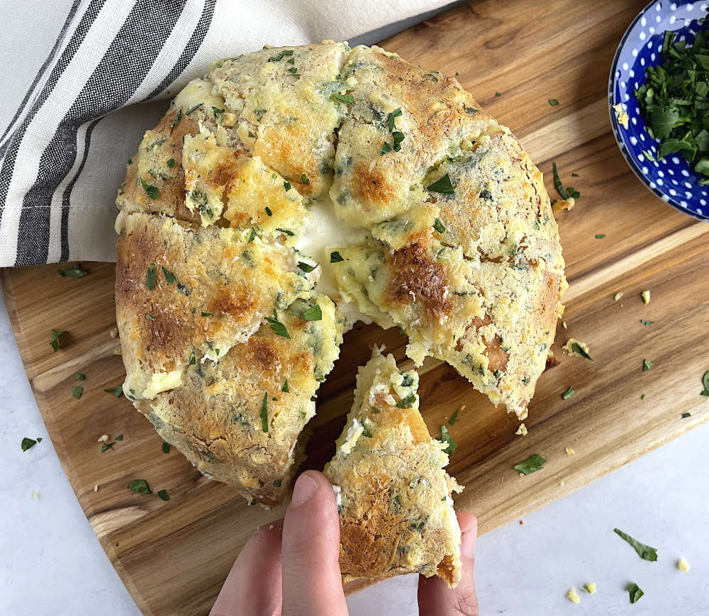 Hand grabbing a piece of bread from the loaf